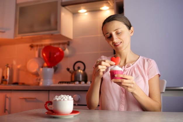 Ein verliebtes Mädchen bereitet Cupcakes für einen geliebten Menschen zum Valentinstag zu und dekoriert das Dessert mit Herz. Eine schöne und köstliche Liebeserklärung.