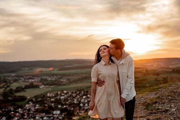 Ein verliebtes Paar, ein Mann und ein Mädchen stehen bei Sonnenuntergang auf einem Berg und umarmen und küssen sich