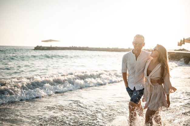 Ein verliebtes Paar geht am Strand am Meer spazieren. Junge Familie bei Sonnenuntergang am Mittelmeer. Sommerferienkonzept