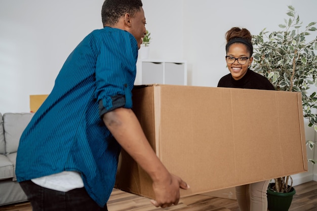 Ein verliebtes Paar trägt schwere Kisten mit gepackten Sachen aus dem Haus, während es in eine neue Wohnung zieht