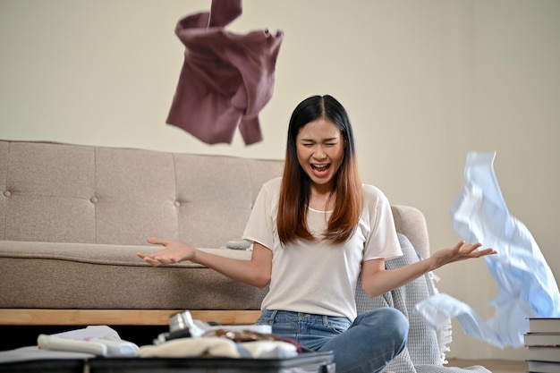Ein verrücktes asiatisches Mädchen wirft ihre Kleidung in die Luft, während sie zu Hause ihren Koffer packt