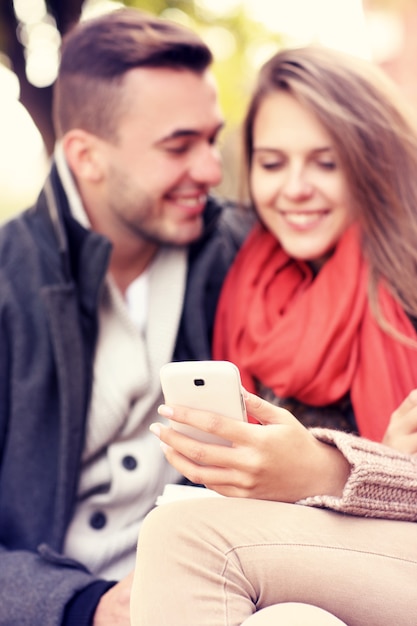 Ein verschwommenes Porträt eines jungen Paares auf einer Bank mit Smartphone im Park