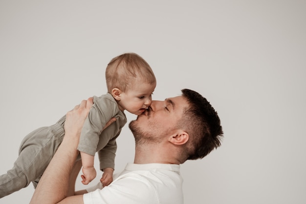 Ein Verwandter eines kleinen Kindes freut sich über sein erstes Treffen, küsst das Baby auf die Wange, hält es hoch in den Armen, ein Foto, das in einem hellen Raum auf weißem Hintergrund aufgenommen wurde