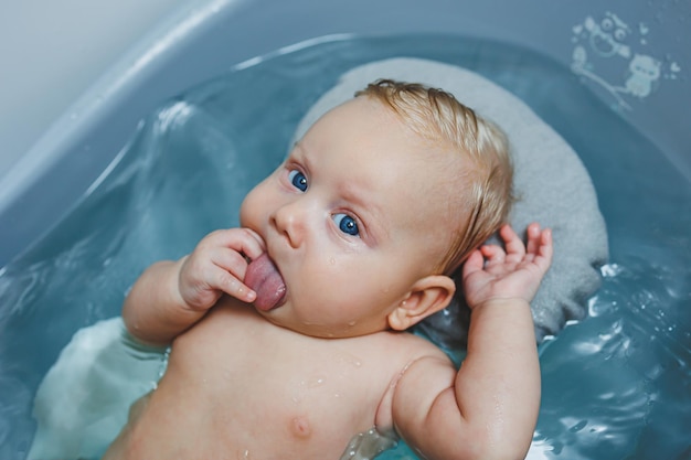 Ein viermonatiger kleiner Junge badet in einer Badewanne, während er auf einem Stand liegt und sich um ein Neugeborenes kümmert, das das Baby badet.