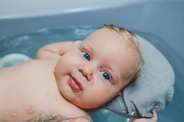 Ein viermonatiger kleiner Junge badet in einer Badewanne, während er auf einem Stand liegt und sich um ein Neugeborenes kümmert, das das Baby badet.