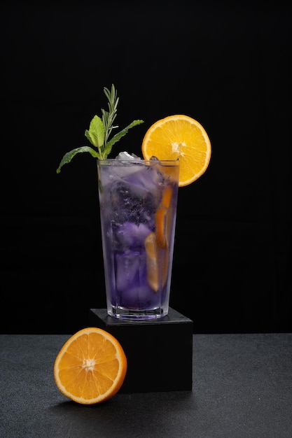 Ein violettes Cocktailglas, das mit Orange und Minze auf dunklem Hintergrund dekoriert ist