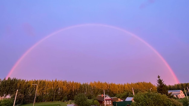 Ein voller Regenbogen vom Dach des Hauses über den Wald und die Häuser Double Rainbow