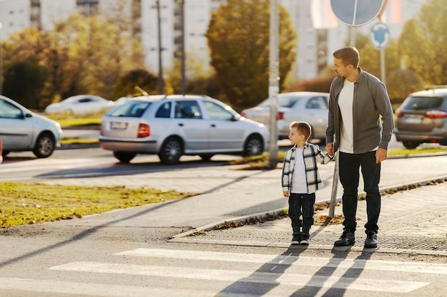 Ein vorsichtiger Vater hält seinen Sohn an der Hand und schaut sich um, während er eine Straße überquert