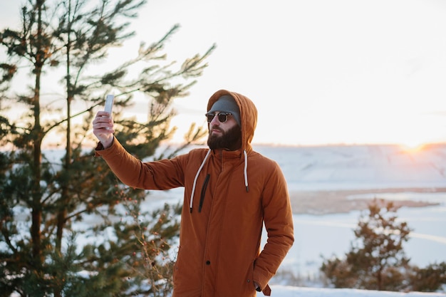 Ein Wanderer genießt den Sonnenuntergang in den Winterbergen und macht ein Foto mit seinem Handy