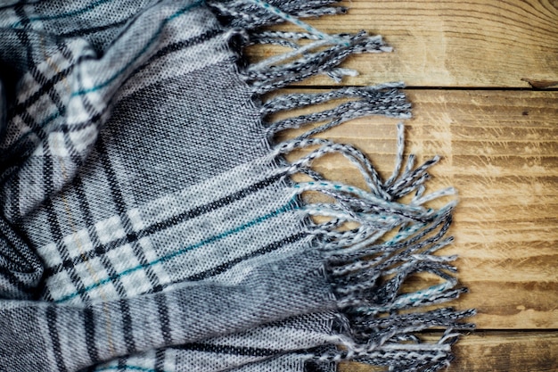 Ein warmer karierter Schal mit Fransen liegt auf hellem Holzhintergrund Das Konzept von Komfort und Wärme