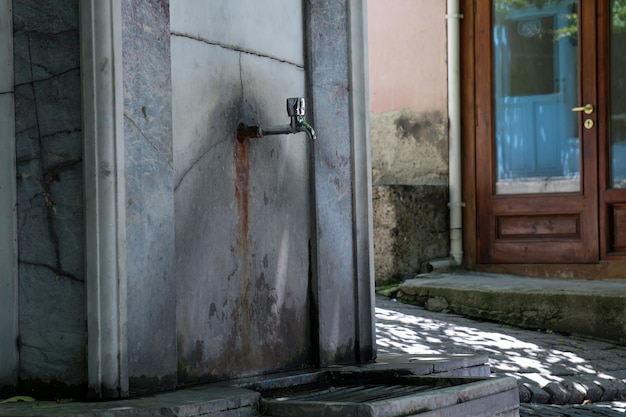 Ein Wasserhahn befindet sich außerhalb eines Gebäudes mit einer Tür im Hintergrund.