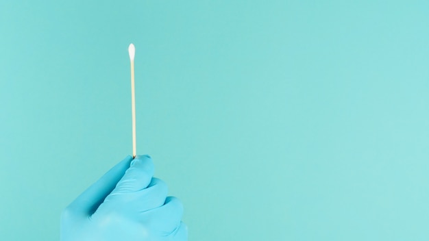 Ein Wattestäbchen für den Tupfertest in der Hand mit blauen medizinischen Handschuhen oder Latexhandschuh auf mintgrünem oder Tiffany Blue background.covid-19-Konzept