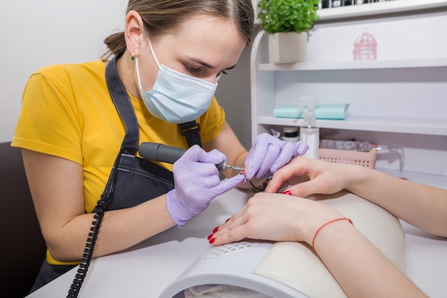 Ein weiblicher Meister verwendet eine elektrische Nagelhautmaschine während einer Maniküre in einem Salon. Hardware-Maniküre-Nahaufnahme. Handpflegekonzept.