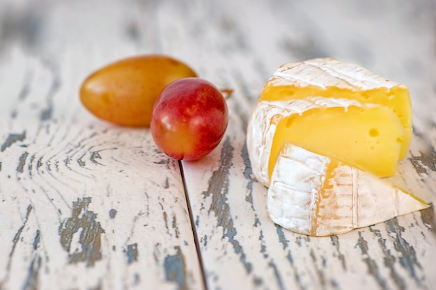 Ein weicher gereifter Camembert-Käse und Trauben auf einem alten Holzbrett.