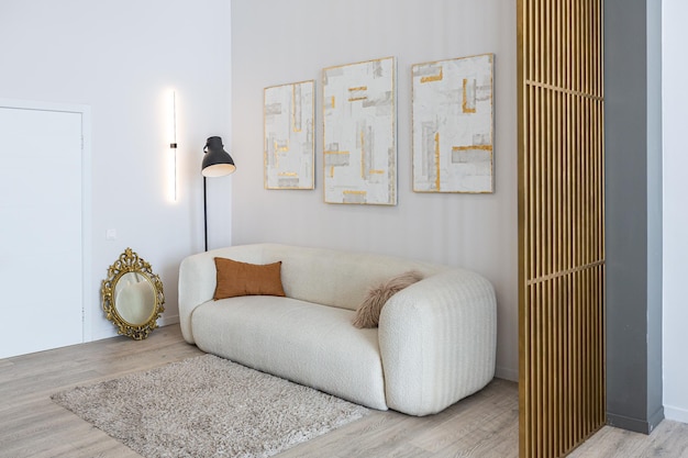 Ein weiches, bequemes Sofa mit Fußbodenlampe ist eine offene Wohnung im modernen Stil mit hellen Wänden und Holzböden und einer stilvollen goldenen Trennwand