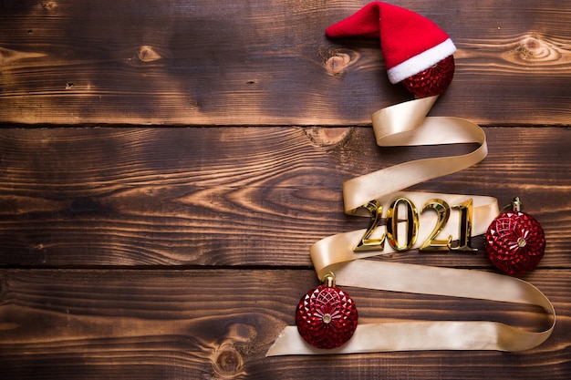 Foto ein weihnachtsbaum aus goldband mit den nummern 2021 ist mit roten luftballons auf dunklem holzhintergrund geschmückt. flach liegen. platz für text. neues jahr, weihnachtsmütze.