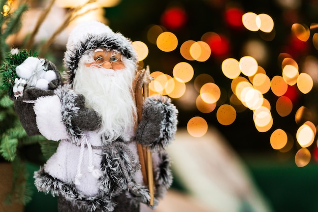 Ein Weihnachtsmann-Spielzeug in einem weißen Anzug steht auf einem dunklen Hintergrund mit Bokeh