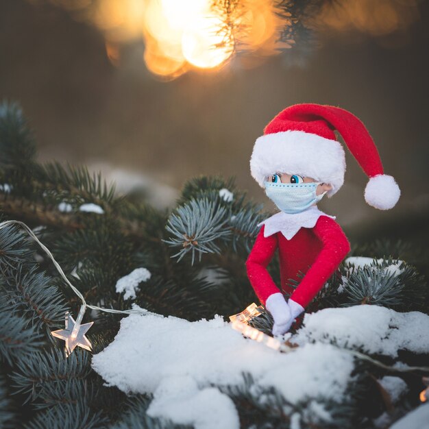 Ein Weihnachtsspielzeug mit Maske sitzt auf den Zweigen eines schneebedeckten Baumes mit einer Girlande funkelnden Sternen