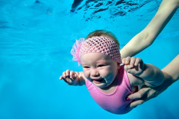 Ein weinender Säugling in den Armen seiner Mutter unter Wasser im Kinderbecken