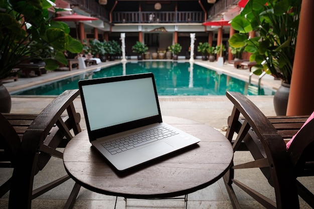 Ein weißer Laptop auf Holztisch-Swimmingpool-Hintergrund