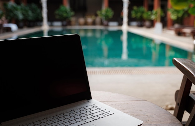 Ein weißer Laptop auf Holztisch-Swimmingpool-Hintergrund