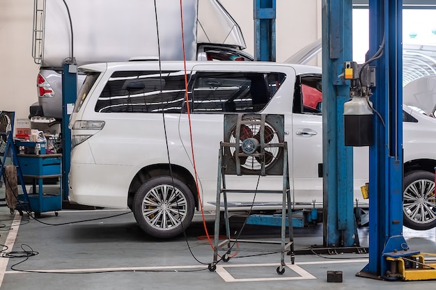 Ein weißer Minivan befindet sich auf einer Hebebühne für Autos zur Reparatur in einem Autowerkstatt-Shop