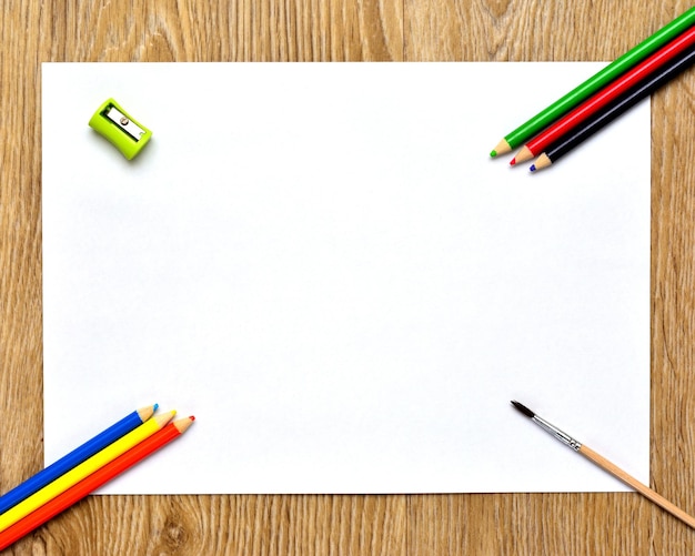 Ein weißes Blatt Papier Buntstifte und ein Pinsel zum Zeichnen auf einem Holzhintergrund