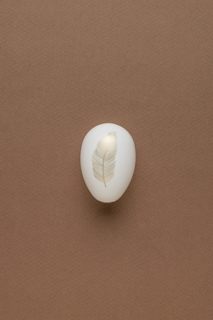 Ein weißes Ei mit goldenem Federmuster auf braunem Hintergrund Minimales Osterkonzept Flach lag