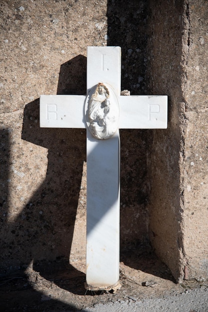 Ein weißes Marmorkreuz mit dem Bild der Jungfrau ruht in einer Ecke eines Friedhofs