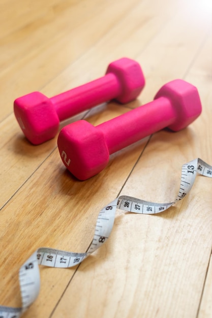 Foto ein weißes messband, das neben zwei kleinen rosa hanteln auf dem holzboden eines heim-gymnasiums liegt