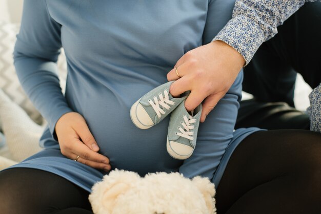 Ein werdender Vater hält blaue Turnschuhe eines ungeborenen Babys auf dem Bauch seiner schwangeren Frau