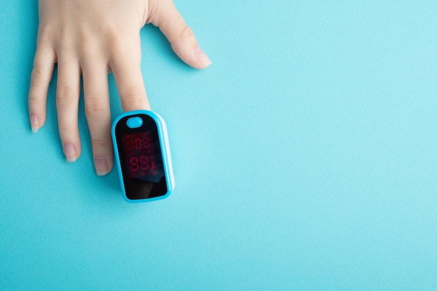 Ein wesentliches medizinisches Gerät für Hypoxie Weiblicher Finger in einem Pulsoximeter auf blauem Hintergrund mit Copyspace