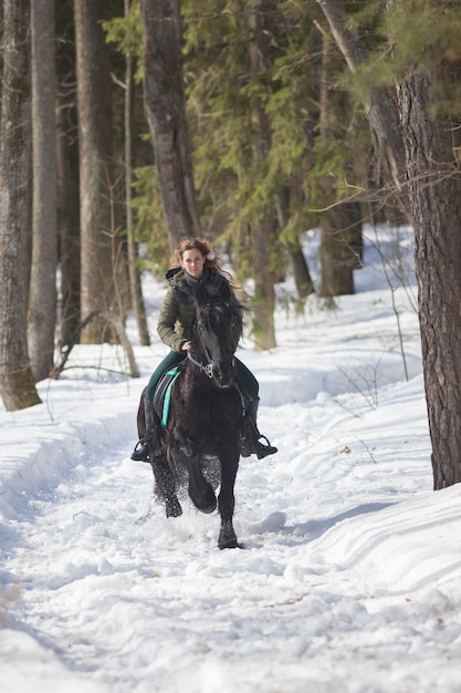 Ein Winterwald eine Frau mit langen Haaren, die auf einem dunkelbraunen Pferd reitet