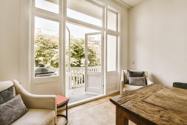 Ein Wohnzimmer mit weißen Wänden und Holzboden. Eine offene Terrassentür führt zum Balkon