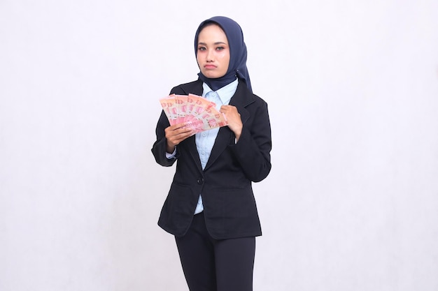 Ein wunderschönes asiatisches Büro-Mädchen, das einen Hijab trägt, steht traurig da und verdient und trägt Rupien aus dem Handel