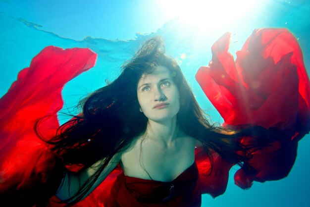 Foto ein wunderschönes, außergewöhnliches mädchen schwimmt unter wasser mit einem roten tuch und offenem haar