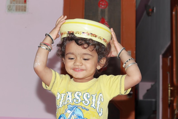 Foto ein wunderschönes indisches kind spielt mit einer plastikbox auf dem kopf.