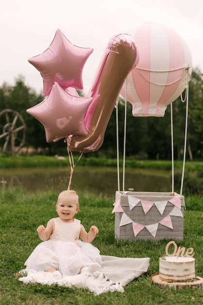 Ein wunderschönes kleines Mädchen in einem Korb mit Ballon und Kuchen feiert ihren ersten Geburtstag