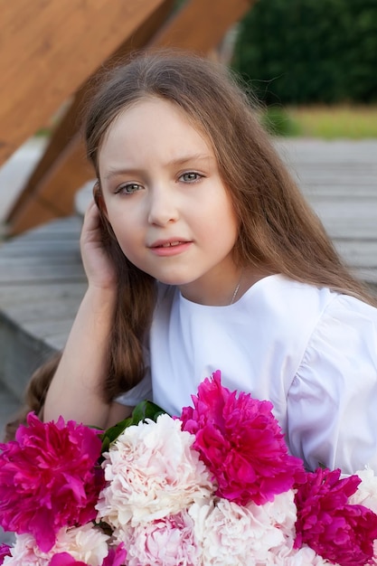 Ein wunderschönes kleines Mädchen mit einem Strauß Pfingstrosen in den Händen auf einem Sommerfeld Fotoshooting im Frühlingsgarten unter freiem Himmel