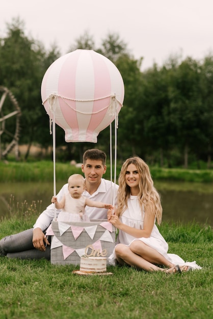 Ein wunderschönes kleines Mädchen mit Mama und Papa in einem Korb mit Ballon und Kuchen feiert ihren ersten Geburtstag