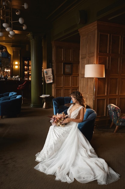 Ein wunderschönes Model-Mädchen in einem luxuriösen Hochzeitskleid, das in einem Vintage-Sessel im luxuriösen Interieur sitzt