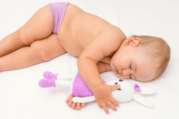 Ein wunderschönes Neugeborenes im Alter von 12-17 Monaten schläft und umarmt ein gestricktes Kaninchenspielzeug.