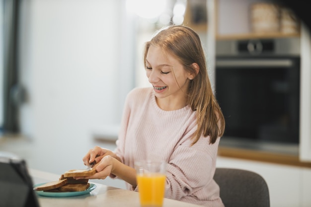 Ein wunderschönes Teenager-Mädchen, das in ihrer Küche frühstückt und den sonnigen Morgen genießt.