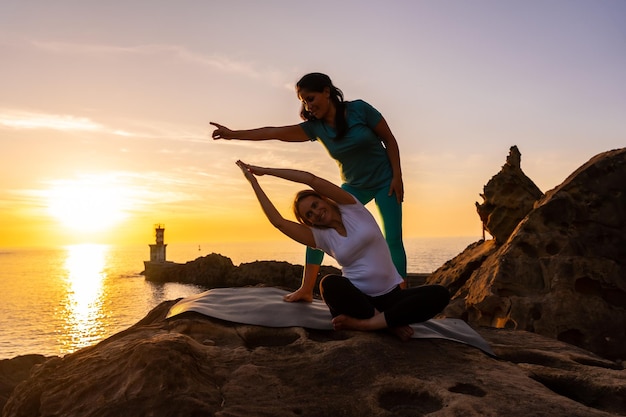 Ein Yogalehrer, der mit dem Schüler in der Natur am Meer bei Sonnenuntergang arbeitet, gesundes und naturistisches Leben im Freien, Pilates