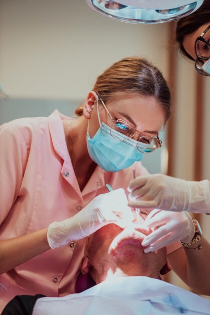 Ein Zahnarzt führt mit Hilfe eines Kollegen eine Operation am Kiefer eines älteren Patienten in einer modernen Zahnklinik durch. Foto in hoher Qualität