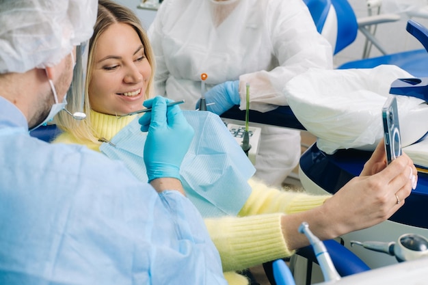 Ein Zahnarzt mit Schutzmaske sitzt neben einem Patienten und macht während der Arbeit ein Selfie-Foto