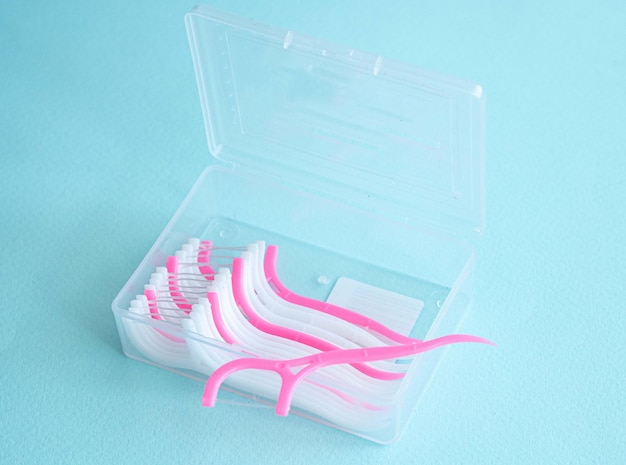 Ein Zahnfaden mit einem Plastikzahnstocher in einem transparenten Plastikbehälter auf einem Blau