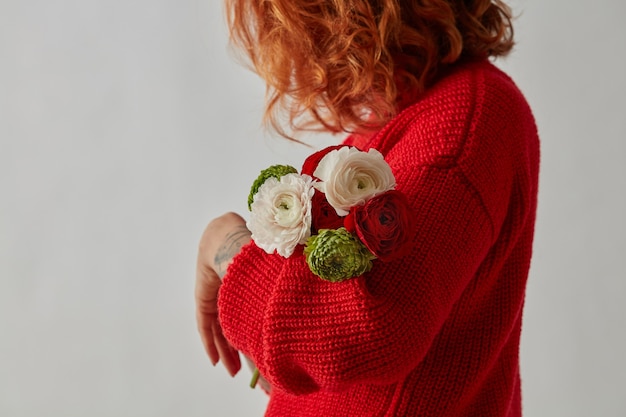 Ein zarter Strauß bunter Blumen von Ranunculus wird von einem Mädchen in einem roten Strickpullover auf grauem Hintergrund mit einer Kopie des Raumes gehalten. Geschenk zum Muttertag