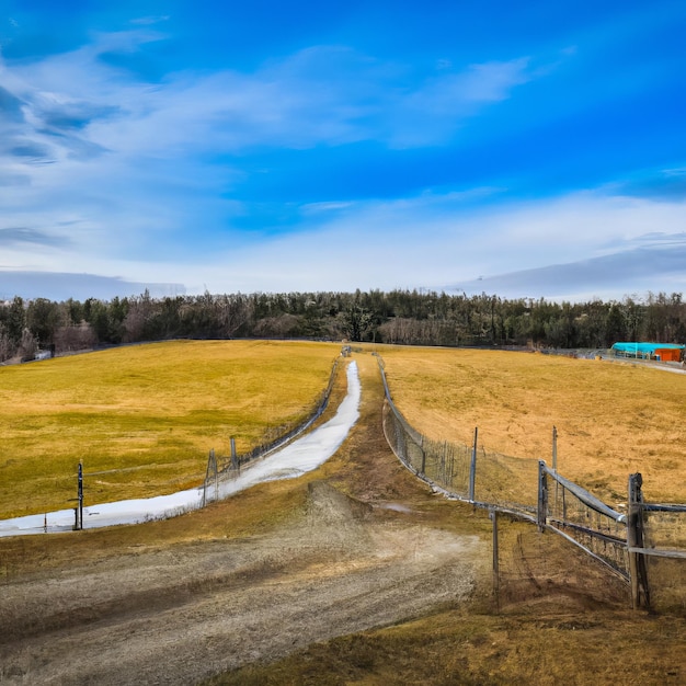 Ein Zaun auf einem Feld mit blauem Himmel und einem Haus im Hintergrund.