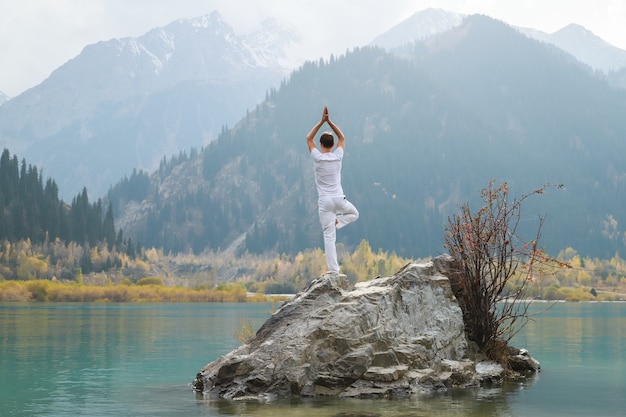 Ein Zen-Mann in Weiß praktiziert Yoga in der Natur. Pose Vrikshasana oder Baumpose.